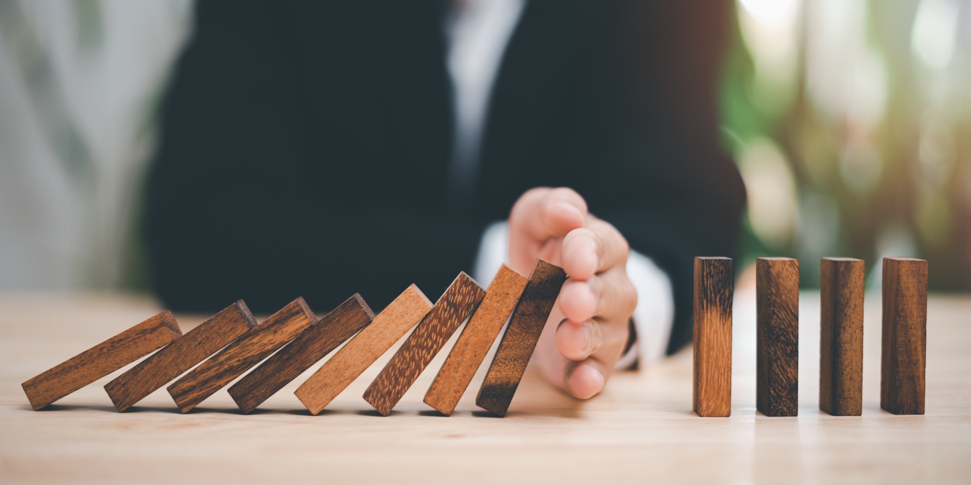A hand stopping a row of falling wooden blocks.